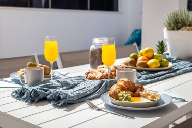 Güneşli bir teras masasında meyve suyu ve kruvasanla taze servis edilmiş kahvaltı..