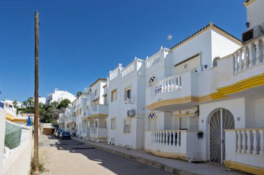 Balkonları, korkulukları ve dekoratif sarı süslemeleri olan beyaz Akdeniz tarzı dairelerle dolu sessiz bir cadde..