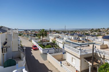 Mahalleye ve uzak bir lagüne bakan beyaz korkuluklara, palmiye ağaçlarına ve mavi çatılara bakan bir çatı..