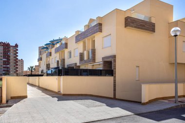 Yeni inşa edilmiş sarı tonlu evler, temiz hatlar, modern tasarım ve balkonlarda süslü ahşap paneller..