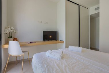 Beyaz çarşafları, düz ekran televizyonu ve kayan dolabı olan basit ve temiz bir yatak odası..