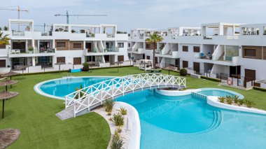 Beyaz kemerli köprüsü, tropikal peyzajı ve çimenliği çevreleyen modern alçak katlı apartmanları olan geniş bir tatil yeri..