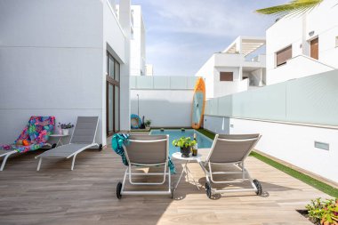 Güneşli yataklı zemin katlı havuz sahnesi, kürek tahtası ve temiz bir avluda gölgeli oturma alanı..