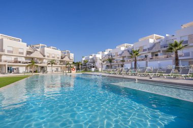 Havuzun geniş manzarası, beyaz modern binalar ve canlı bir gökyüzü altında yemyeşil..