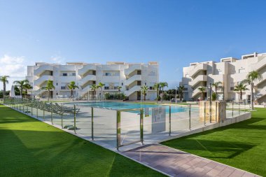 Yeşil yapay çimleri, cam çitleri ve çok katlı modern apartmanları olan güvenli havuz bölgesi..