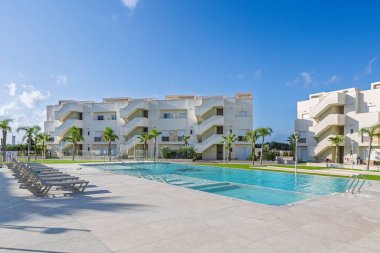 Geniş havuzlu, palmiye ağaçlı ve açık havada dinlenmek için sandalyeli bir sitede güneşli bir gün..