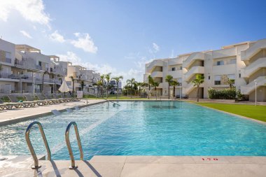 Güneş yatakları ve modern dairelerle çevrili metal basamaklı yüzme havuzları ve su altı şezlongları..