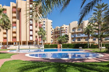 Kavisli yolları, yeşil çimenleri ve güneşli bir komplekste Akdeniz mimarisi olan avuç içi çizgili havuz alanı..