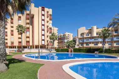 Havuz manzarası geniş palmiye ağaçları, modern daireler ve açık gökyüzü, gayrimenkul tanıtımı için ideal..