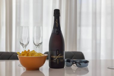 Freixenet Cava şişesi, iki bardak, bir kase cips ve parlak mutfak tezgahında güneş gözlüğü..
