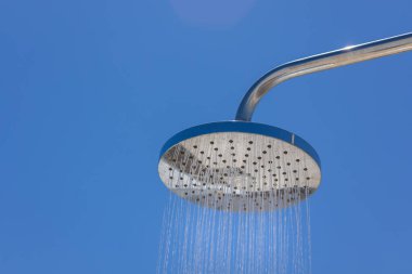 Modern bir açık hava krom duş başlığının yakın çekimi açık mavi bir yaz gökyüzünün altında su püskürtüyor..
