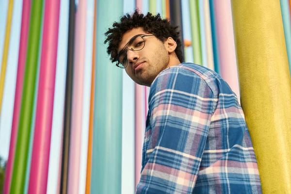 stock image Low angle of the pensive middle eastern man wearing eyeglasses looking at the camera standing near the colorful wall. Human lifestyle concept 