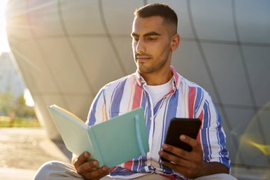 Düşünceli yakışıklı ortadoğu öğrencisi, sınav hazırlığı, üniversite kampüsünde kitap okuma. Eğitim kavramı                         