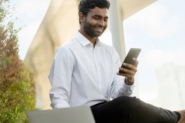Приваблива Усмішка Індійського Чоловіка Який Тримає Мобільний Телефон Допомогою Ноутбука — стокове фото