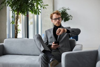 Dalgın yakışıklı işadamı saat kontrolüne bakıyor. Ofiste birini bekliyor.  