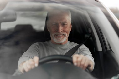 Portrait of a Caucasian handsome confident gray-haired elderly man driver, driving on the road in a new car. Seat belt, safety driving concept. Auto insurance and compliance with the rules of the road