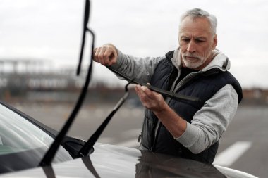 Portrait of senior man technician checking, changing, mounting new windscreen wipers by himself on the dealership car station