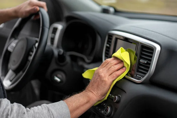 Details: selective focus on hands of a senior man, using a yellow microfiber cloth, applying wax, waxing, wiping and polishing the dashboard in the car interior. Car wash, detailing and valeting