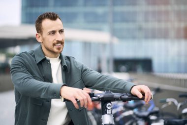 Genç, gülümseyen bir turist, yolda elektrikli scooter kullanıyor ve başka tarafa bakıyor. Çevre taşımacılığı kavramı 