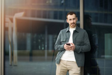 Akıllı telefonu elinde tutan kendine güvenen adam mobil uygulama kullanarak sokaktaki kameraya bakıyor, uzayı kopyalıyor. Çekici stil hipster adam online alışveriş, mobil bankacılık konsepti 