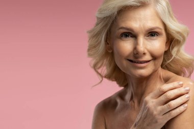 50-55 yaşlarındaki beyaz kadın yetişkin, kendine güvenen sarışın bir kadın kameraya bakıyor, pembe arka planda üstsüz poz veriyor. Uzayı kopyala Yaşlanma karşıtı güzellik konsepti