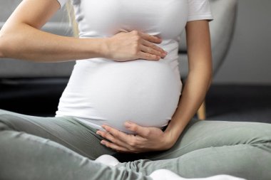 Close up of pregnant woman touching her belly sitting in lotus pose at home. Pregnancy, motherhood, new life concept 