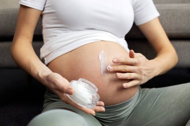 Close-up of pregnant woman applying cream on her belly to prevent stretch marks. Pregnancy, skincare concept 