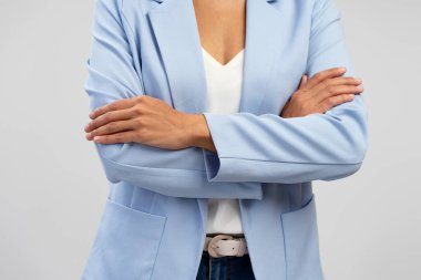 Cropped view of a confident slim young woman in blue casual jacket and denim, keeping her arms crossed, standing isolated over white background. Close-up businesswoman, entrepreneur, sales manager
