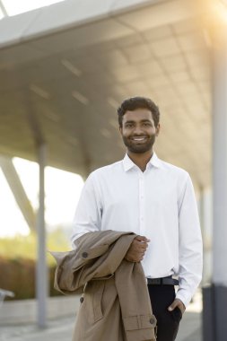Portrait of young smiling asian businessman holding trench coat looking at camera walking on the street