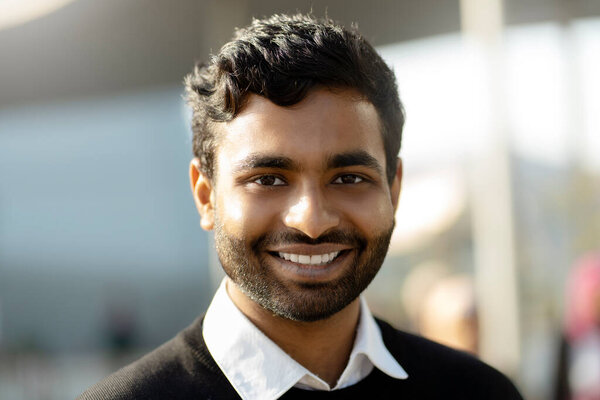 Portrait of smiling confident Indian student looking at camera standing in university campus. Education concept 