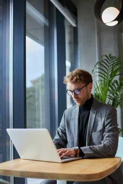 Caucasian confident young man in formal suit and eyeglasses, entrepreneur, sales manager typing on laptop keyboard while telecommuting from a modern office. People, business and freelance work concept