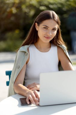 Beautiful confident woman freelancer using laptop computer working online sitting at workplace. Young student studying, learning language, exam preparation outdoors, online education concept
