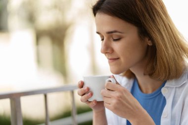 Positive smiling woman drinking coffee at open air cafe. Young happy student having coffee break outdoors. Morning concept