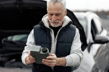 Kafkasyalı kıdemli şoför, kaputu açık bir şekilde arabanın arka planında duruyor ve motordaki yağı doldurmak için bir şişe motor yağını söküyor. Yağ seviyesini kontrol et. Araba bakım konsepti