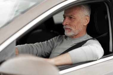Kendine güvenen, pozitif, 60-70 yaşlarında, emniyet kemerini takmış, yeni arabasını sürmekten zevk alan yaşlı bir adamın yakın plan portresi. Güvenli sürüş ve trafik kurallarına uyma.