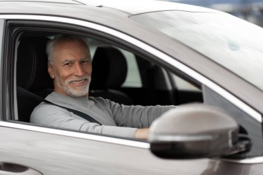 Mutlu Araba Sahibi. Son sınıf öğrencisi, yeni lüks bir araba kullanıyor. Şen şakrak, yaşlı erkek sürücü sürücü sürücü sürücü koltuğunda kemerini bağlayıp, direksiyonu tutuyor ve kameraya bakıp gülümsüyor.