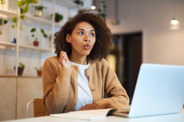Young confident African American woman, gestures with hand, talks by video link, sitting at a desk with laptop in modern office. People, technology, online communication, career, remote work concept