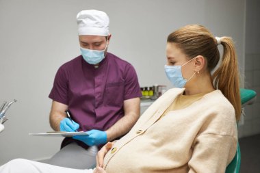 Caucasian young pregnant woman, wearing medical mask, at dentist appointment in dentistry clinic. The concept of a preventive examination by a dentist during pregnancy