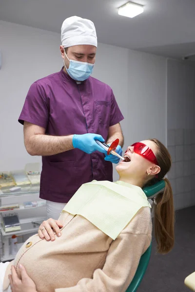 在现代牙科诊所接受牙齿美白治疗的白人年轻孕妇 牙医在诊所为一位年轻漂亮的妇女做了牙齿美白手术 笑得漂亮 — 图库照片