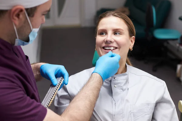 Cosmetic Dentistry. Dentist Office - Caucasian female patient sitting on chair before teeth checkup and teeth whitening bleaching. Doctor checks the tooth color on a comparative scale of veneers.