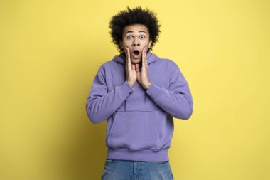 Portrait of young shocked man with open mouth holding hands near face isolated on yellow background. Shopping, sales concept
