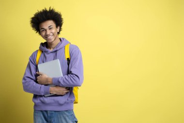 Confident smiling African American student holding laptop isolated on yellow background, copy space. Education concept. Portrait of happy successful man freelancer looking at camera