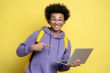 Young happy African American man freelancer using laptop computer, pointing index finger on laptop screen, isolated on yellow background. Smart smiling student studying, online education concept