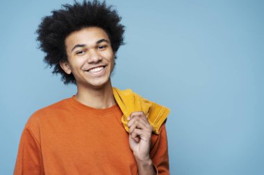 Closeup portrait of smiling African American man wearing stylish clothes isolated on blue background, copy space. Happy smart student with curly hair looking at camera posing for pictures, studio shot
