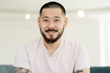 Closeup portrait of young smiling Asian man posing for pictures, looking at camera sitting at home