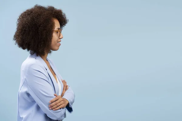Smiling african american female entrepreneur standing isolated on blue background. Happy businesswoman in suit posing arms crossed