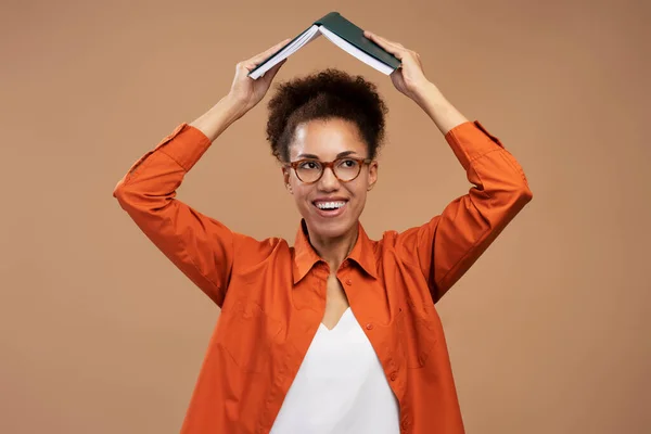 镜片中黑头发的阳性女性的画像 头顶着书本站着 学习和教育 在棕色背景下被隔离的室内拍摄 — 图库照片