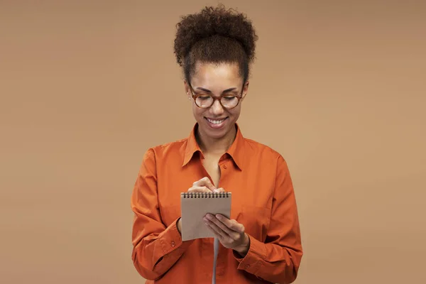 Portrait Smiling African American Woman Writing Notes Isolated Brown Background — Stockfoto
