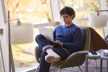 Kendine güveni tam genç bir Latin Amerikalı, başarılı bir iş adamı, şık gözlükler takıyor ve gündelik giysiler giyiyor, online olarak dizüstü bilgisayarda çalışıyor, proje planlıyor, modern bir ofisten iş seyahati yapıyor.