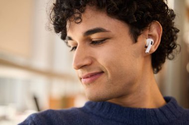 Gülümseyen Latin Amerikalı bir adamın kablosuz kulaklıkla müzik veya online ders yayını dinleyen aşırı yakın plan portresi. Halk Teknoloji Eğitim Şirketi